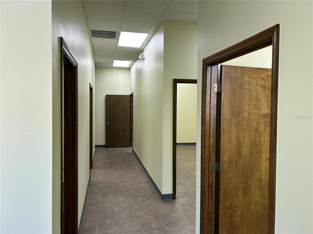 A hallway with tile flooring leads to several wooden doors and a drop ceiling — 4426 NE 83RD ROAD UNIT 4426, WILDWOOD, FL