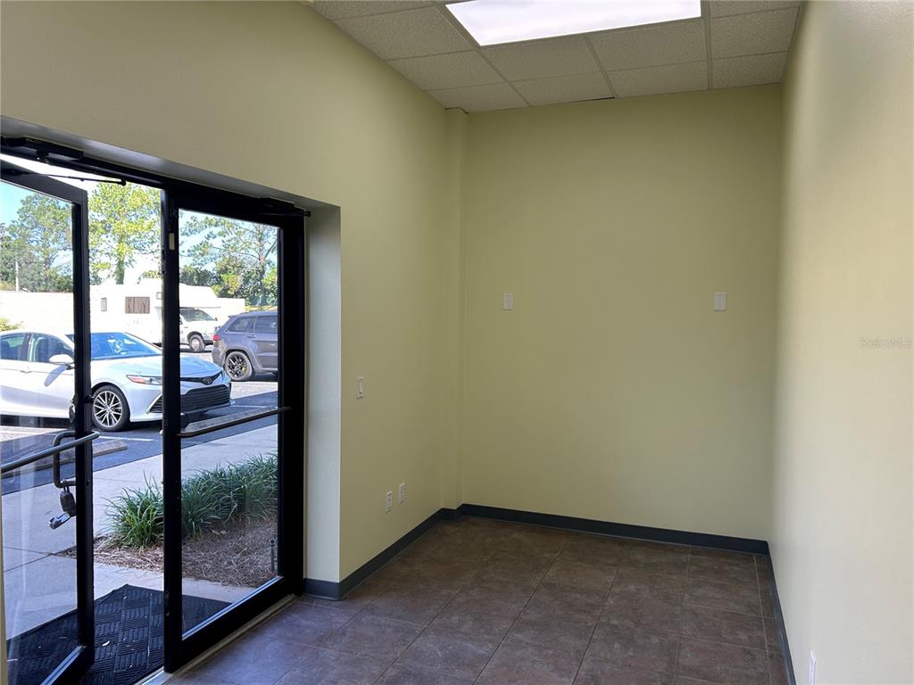 An empty office room features light yellow walls, tile flooring, and a glass entry door — 4426 NE 83RD ROAD UNIT 4426, WILDWOOD, FL