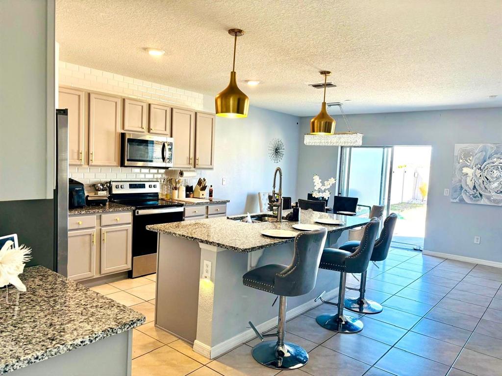 A kitchen features light-colored cabinets, granite countertops, a central island with bar stools, and lighting — 5837 ARLINGTON RIVER DRIVE, LAKELAND, FL
