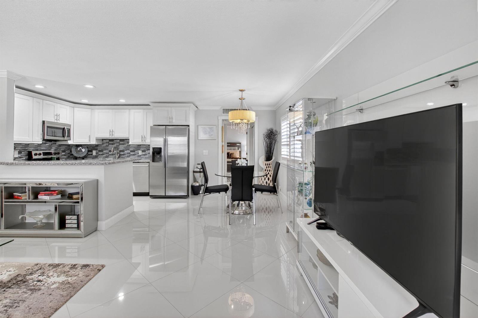 A modern open-concept kitchen and dining area with white cabinetry, stainless appliances, and tile flooring — 102 E Waterford E # 102, Delray Beach FL 33446, DELRAY BEACH, FL