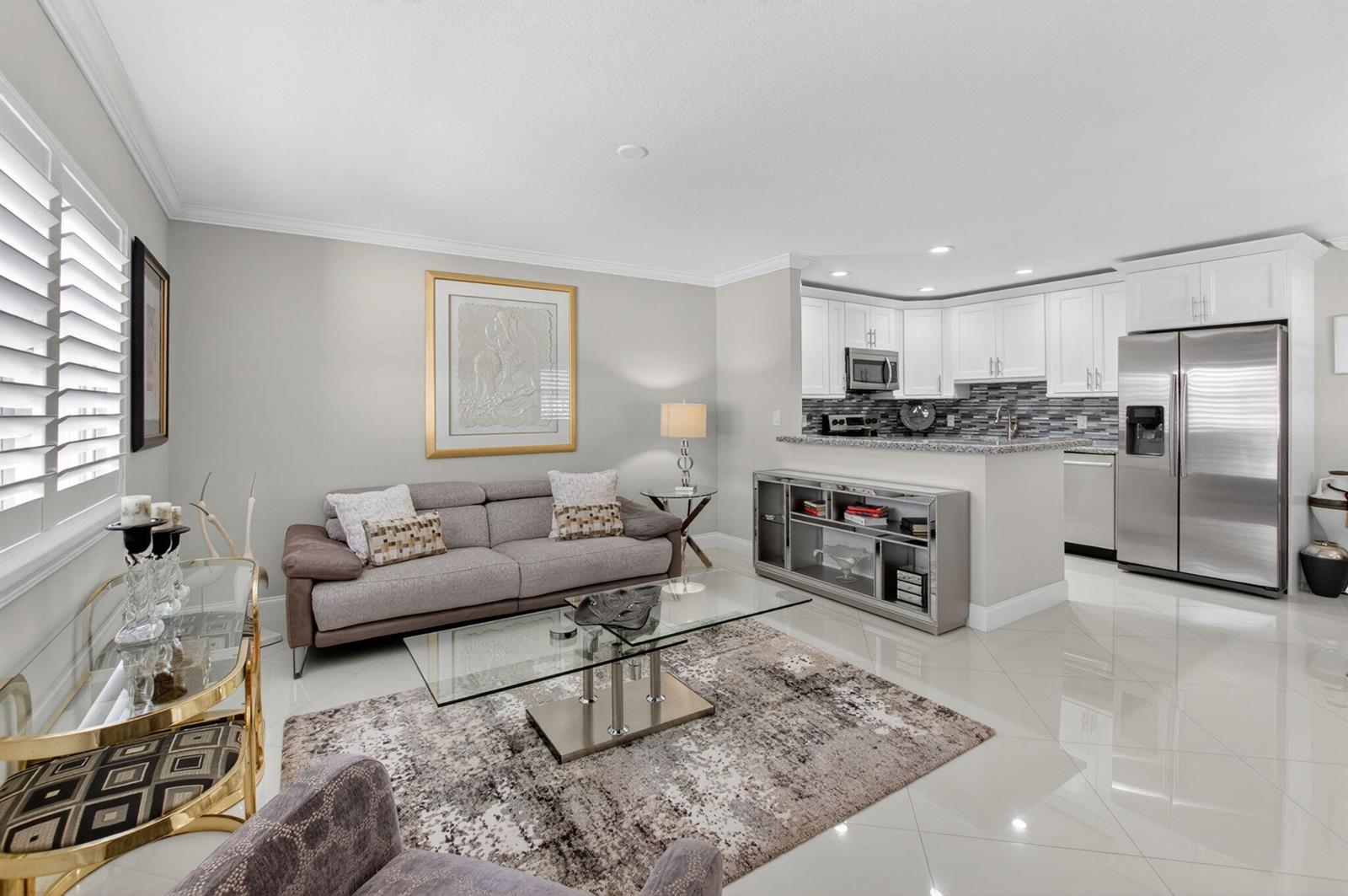 A living room with a grey sofa, glass coffee table, and an open kitchen with white cabinets — 102 E Waterford E # 102, Delray Beach FL 33446, DELRAY BEACH, FL