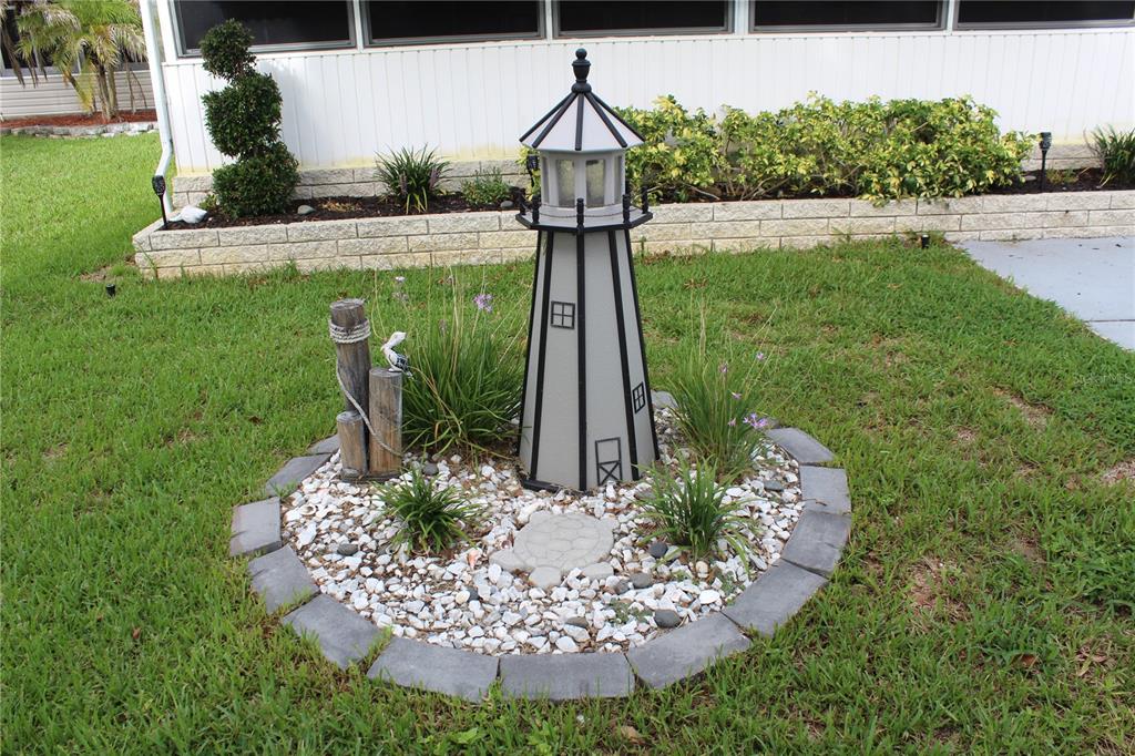 A decorative lighthouse garden ornament sits in a circular, stone-bordered bed on a grassy lawn — 6369 ELMWOOD AVENUE, LAKE WALES, FL