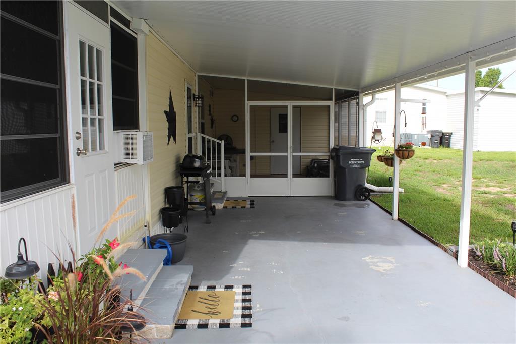 A covered concrete patio features a screened-in porch entrance, a grill, and a trash bin — 6369 ELMWOOD AVENUE, LAKE WALES, FL