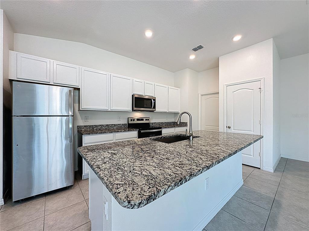 A kitchen features white cabinets, stainless steel appliances, and a granite-topped island with a sink — 707 SCRUB OAK HAMMOCK ROAD, DAVENPORT, FL