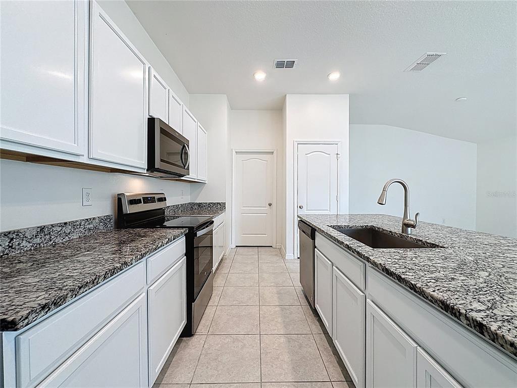 A kitchen features white cabinets, granite countertops, stainless steel appliances, and a central island — 707 SCRUB OAK HAMMOCK ROAD, DAVENPORT, FL