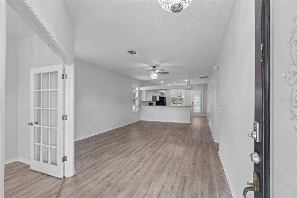 An open-concept living area with light wood-look flooring, white walls, and a kitchen in back — 10207 PORCH STREET, NEW PORT RICHEY, FL