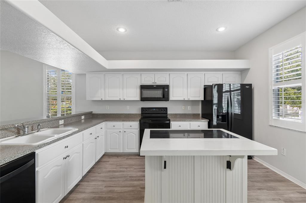 A kitchen with white cabinets, black appliances, a central island, and light wood-look flooring — 10207 PORCH STREET, NEW PORT RICHEY, FL