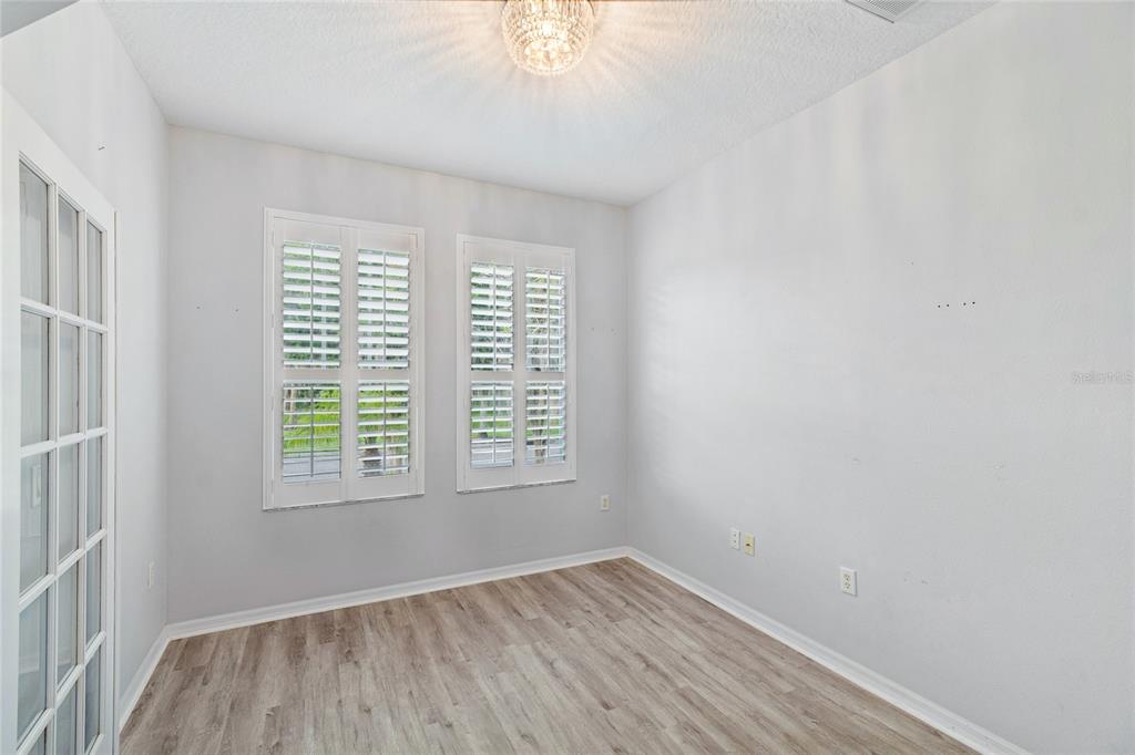 An empty room with light wood-look flooring, white walls, plantation shutters, and a crystal chandelier — 10207 PORCH STREET, NEW PORT RICHEY, FL