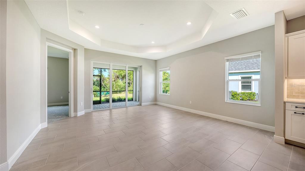 A bright, empty room features light tile flooring, a tray ceiling, and sliding glass doors — 11653 GREAT BROOK LANE, PARRISH, FL