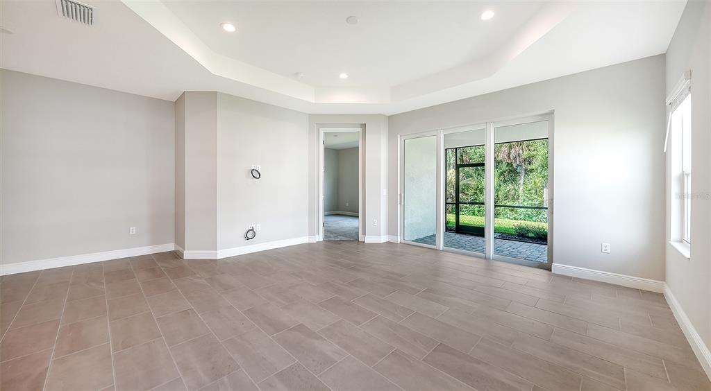 A spacious room with light gray walls, tile flooring, a tray ceiling, and sliding glass doors — 11653 GREAT BROOK LANE, PARRISH, FL