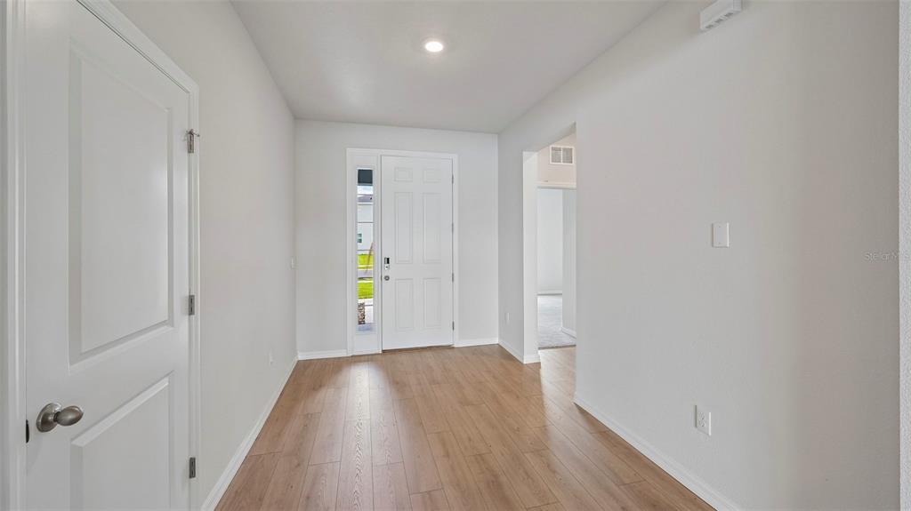 An entryway features light wood-look flooring, white walls, and a white front door — 10405 WOODLAND GARDEN WAY, PARRISH, FL