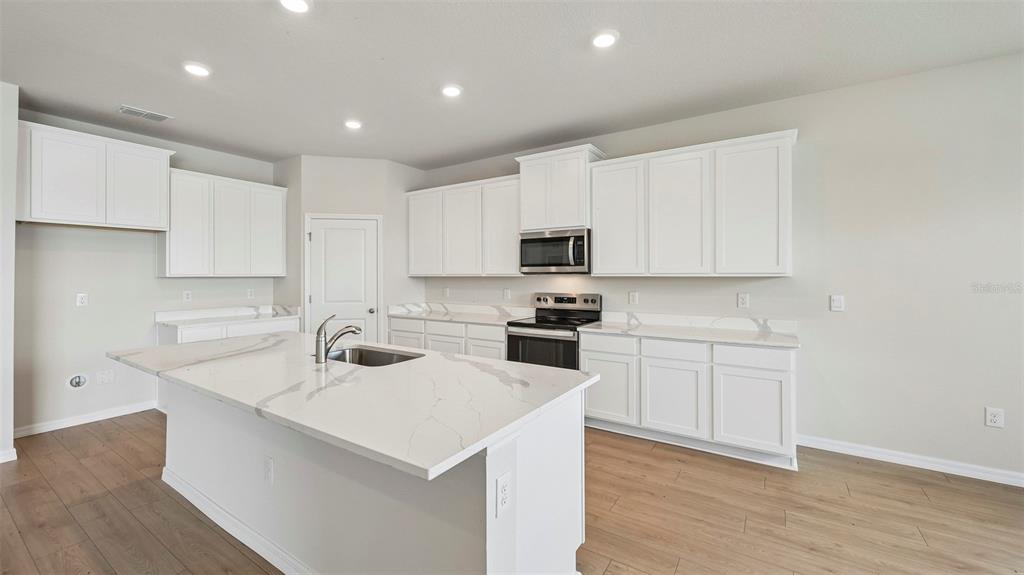 A modern kitchen features white cabinets, a large quartz island with a sink, and wood-look flooring — 10405 WOODLAND GARDEN WAY, PARRISH, FL