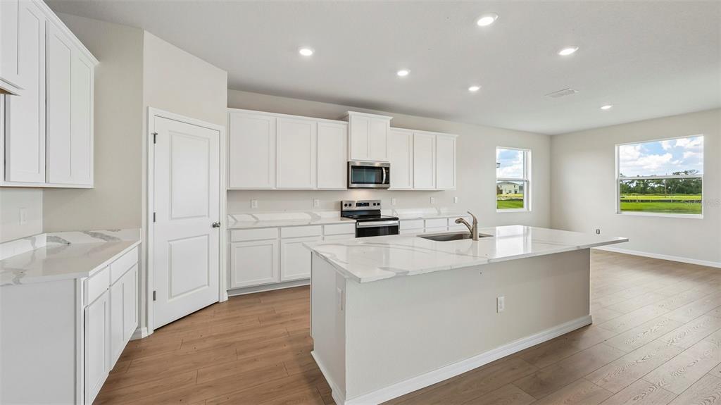 A modern kitchen features white cabinets, a large marble-topped island, and light wood flooring — 10405 WOODLAND GARDEN WAY, PARRISH, FL
