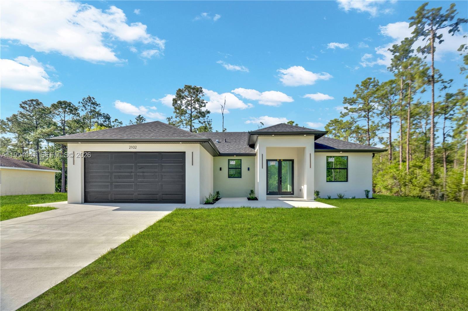 A modern single-story house with a dark garage door, white stucco exterior, and black trim — 2102 E 13th St, Lehigh Acres FL 33972, LEHIGH ACRES, FL