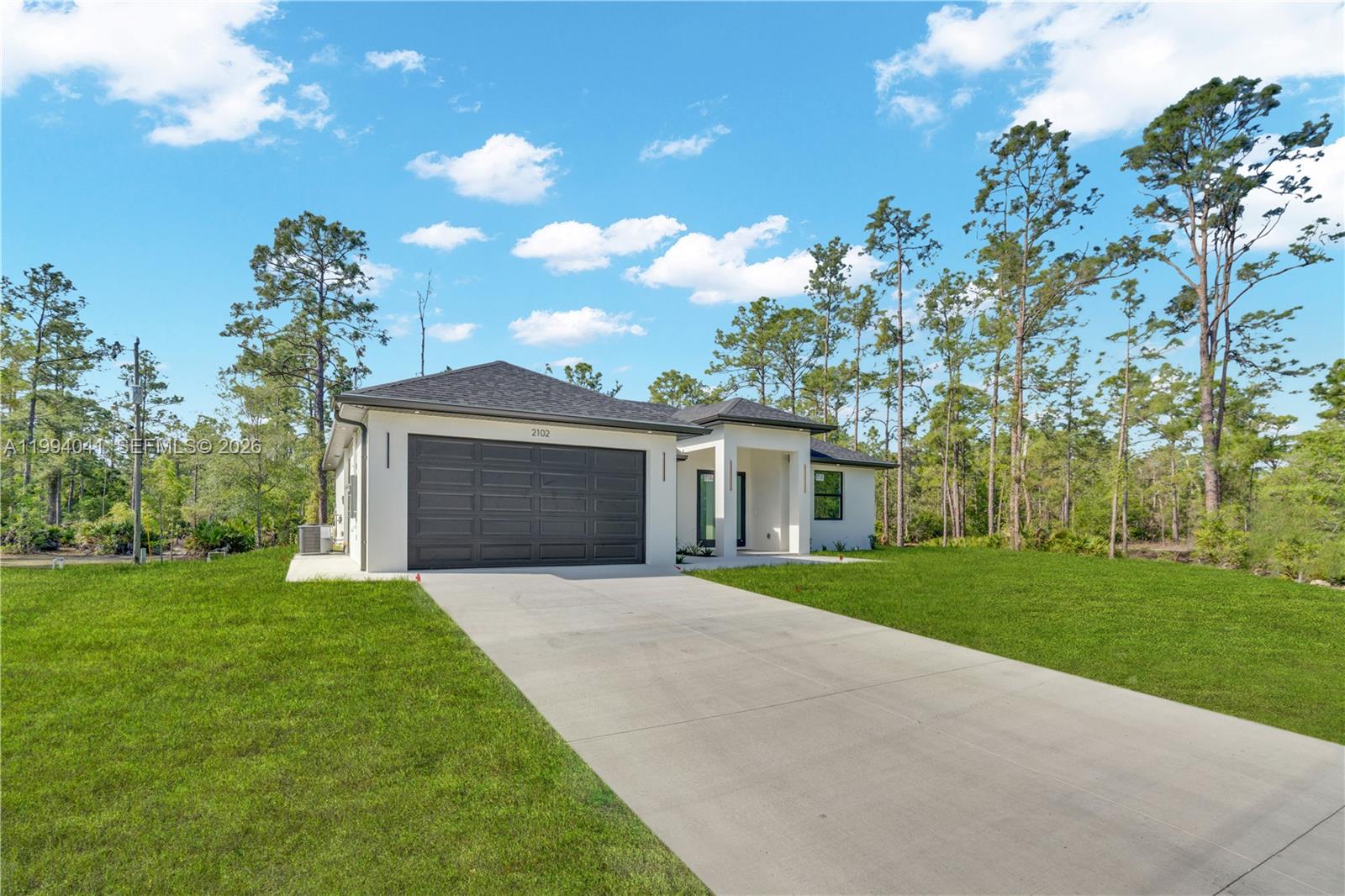 A modern single-story house with a white exterior, dark garage door, and a concrete driveway — 2102 E 13th St, Lehigh Acres FL 33972, LEHIGH ACRES, FL