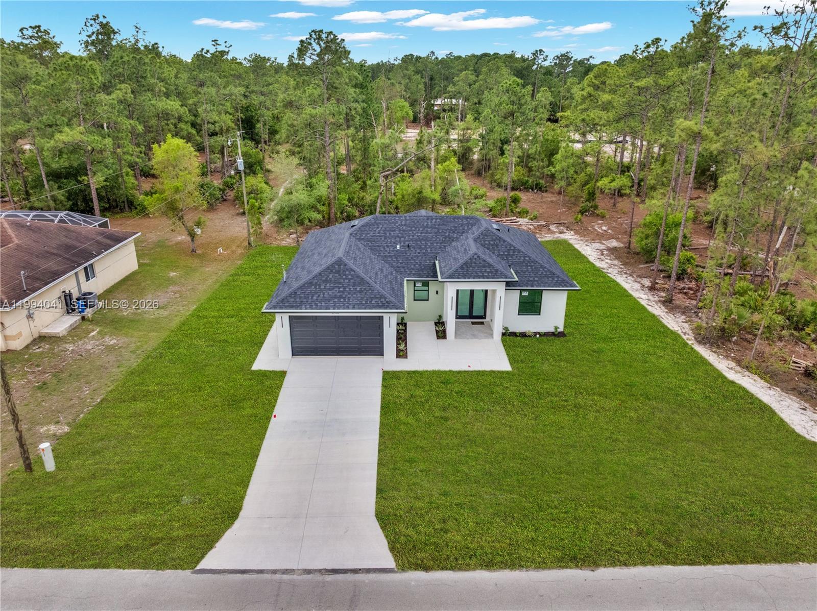 An aerial view shows a modern single-story house with a dark roof and concrete driveway — 2102 E 13th St, Lehigh Acres FL 33972, LEHIGH ACRES, FL