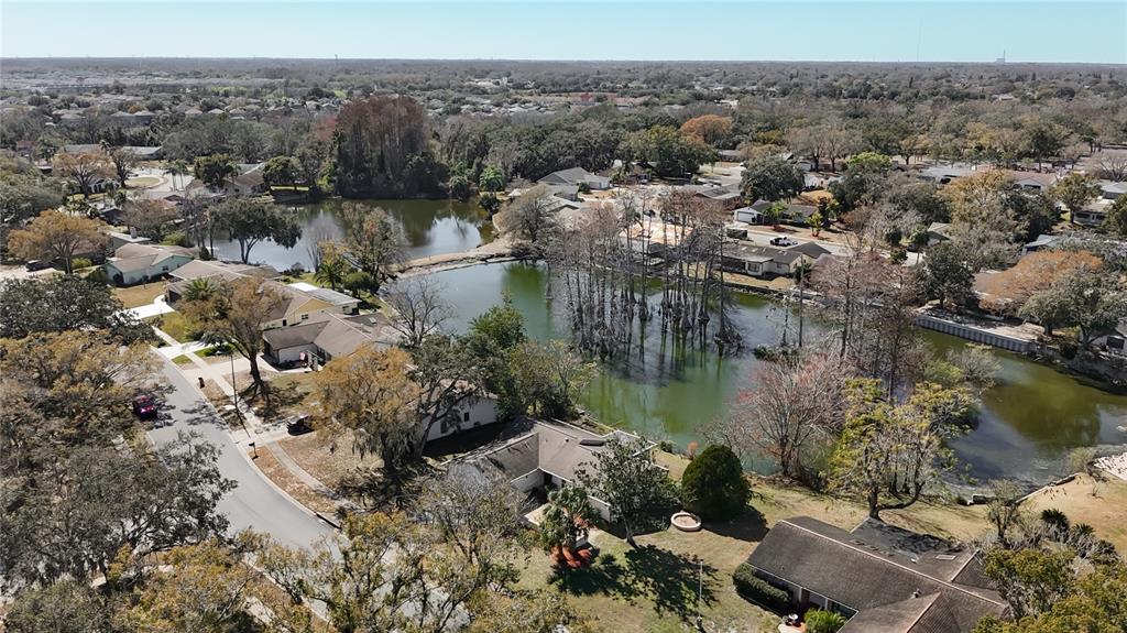 An aerial view shows a residential neighborhood with houses surrounding a large, tree-filled pond — 3845 ERIN BROOK DRIVE, NEW PORT RICHEY, FL