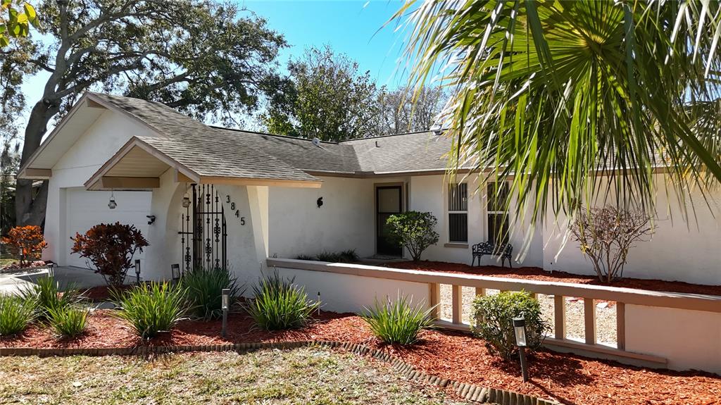 A single-story white house with a garage, a gated entryway, and red mulch landscaping — 3845 ERIN BROOK DRIVE, NEW PORT RICHEY, FL