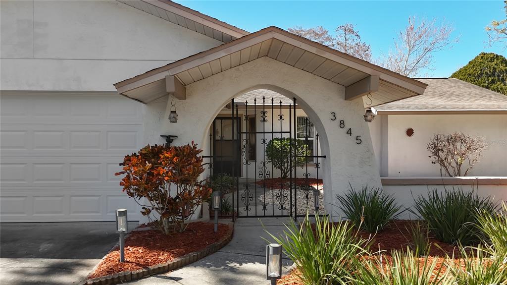 The exterior of a house features a gated courtyard entrance and a white garage door — 3845 ERIN BROOK DRIVE, NEW PORT RICHEY, FL
