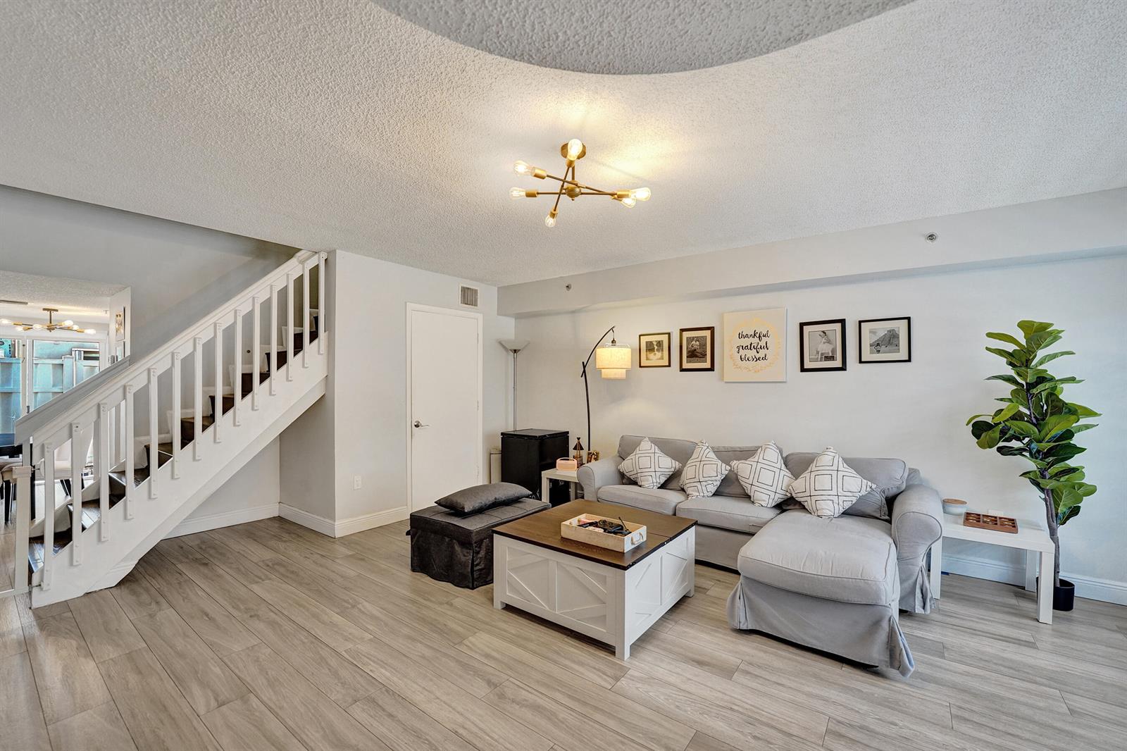 A living room features light wood-look flooring, a grey sectional sofa, and a white staircase — 173 Riviera Circle, Weston FL 33326, WESTON, FL