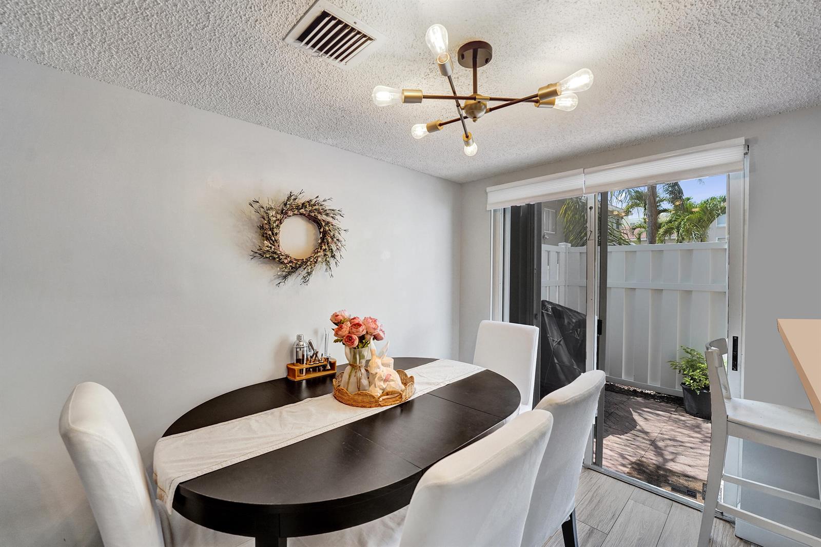 A dining area features a dark oval table, white chairs, a chandelier, and sliding glass doors — 173 Riviera Circle, Weston FL 33326, WESTON, FL
