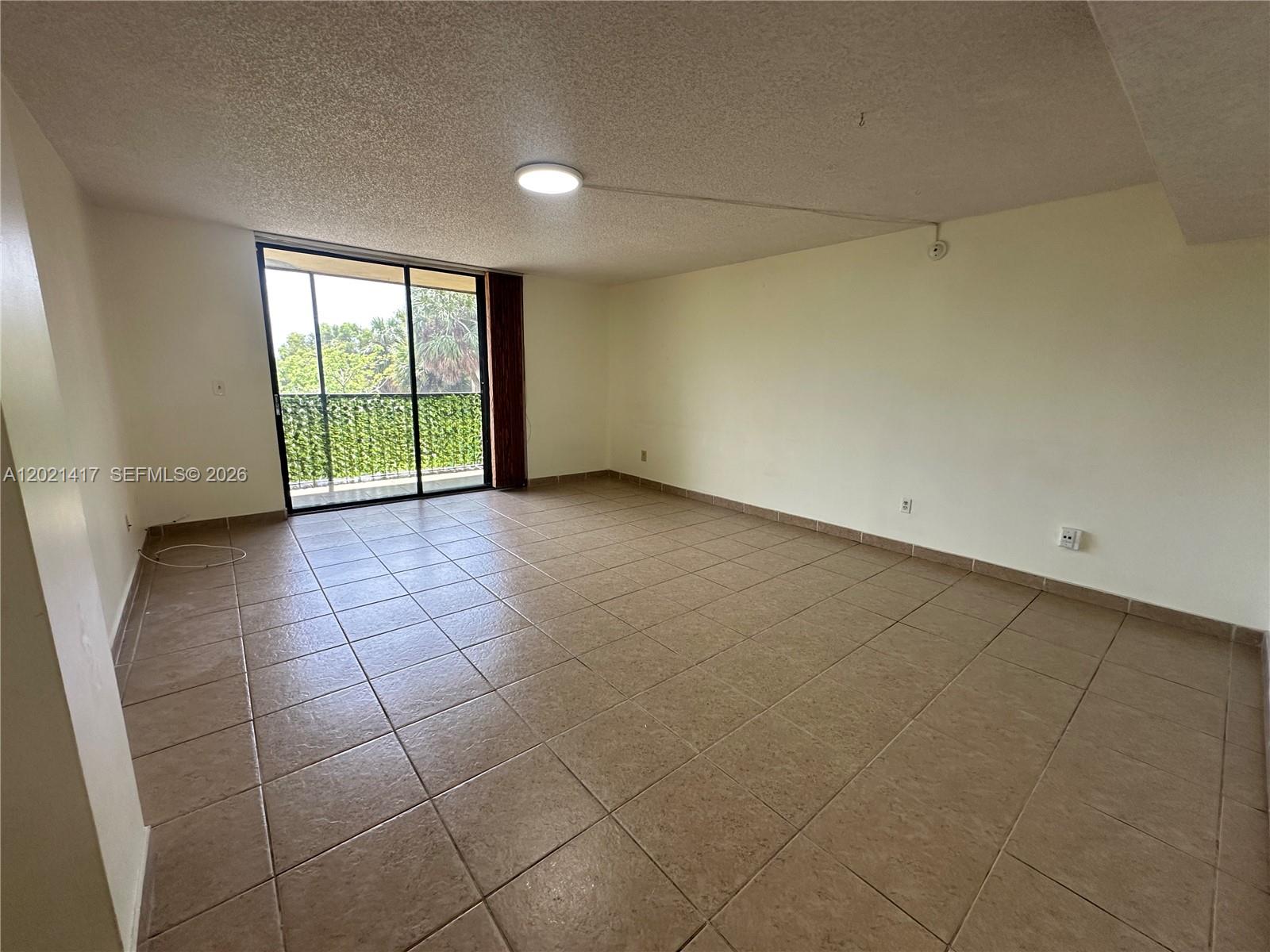 An empty living room features beige tile flooring, a ceiling light, and a sliding glass door — 8635 NW 8th St # 320, Miami FL 33126, MIAMI, FL