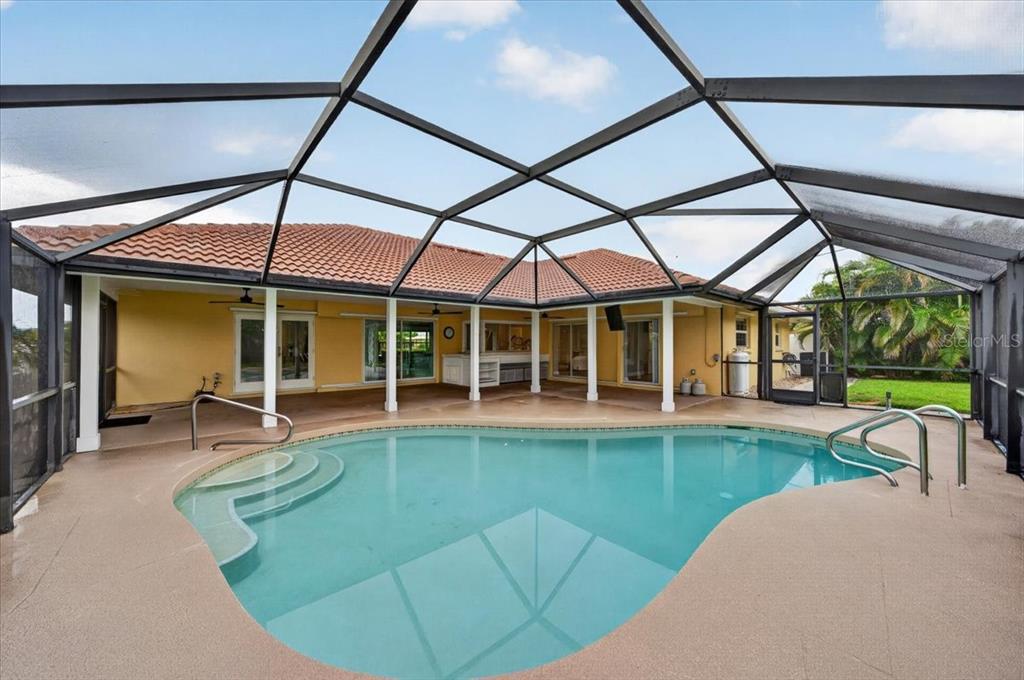 A screened-in swimming pool sits on a patio adjacent to a yellow house with a tiled roof — 100 MATISSE CIRCLE W, NOKOMIS, FL