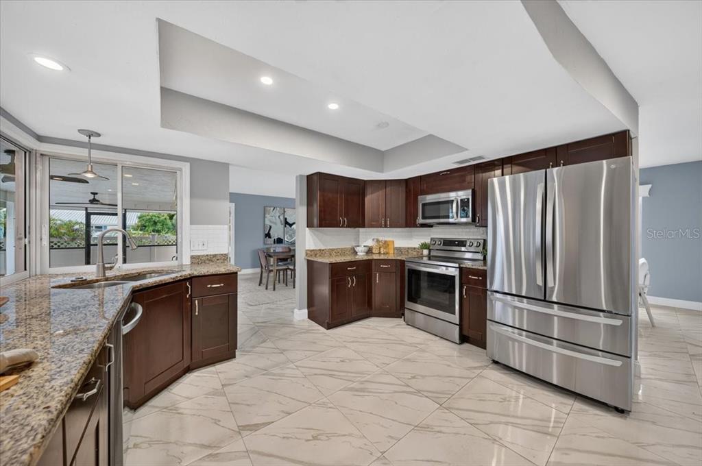 A kitchen features dark wood cabinets, granite countertops, stainless steel appliances, and light tile flooring — 100 MATISSE CIRCLE W, NOKOMIS, FL
