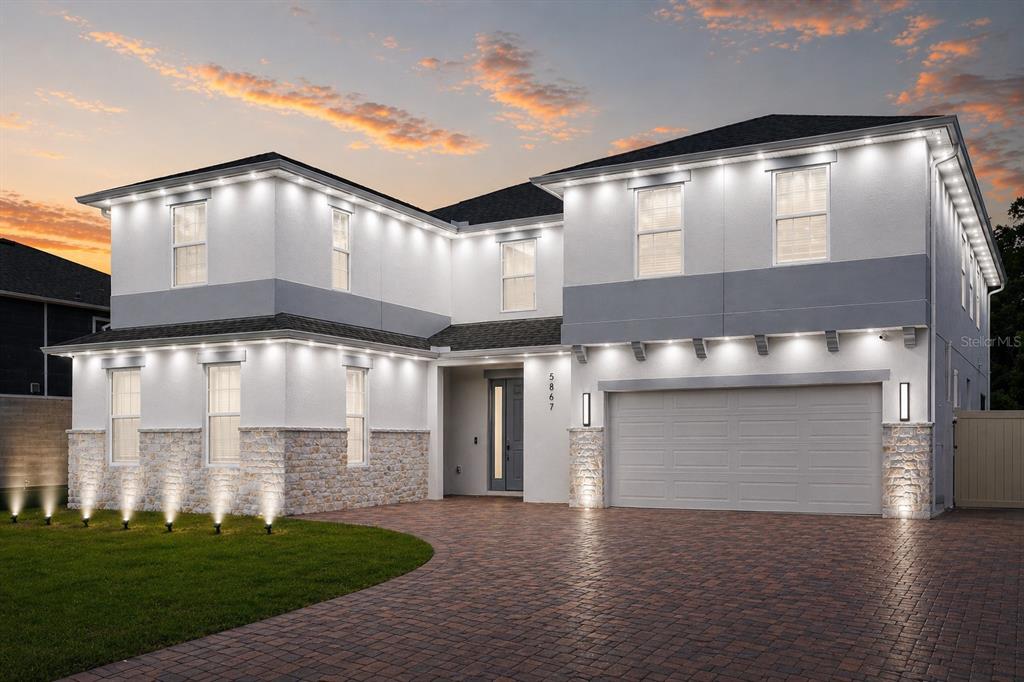 A two-story house with white stucco, stone accents, and exterior accent lighting at dusk — 5867 SIERRA CROWN STREET, MOUNT DORA, FL