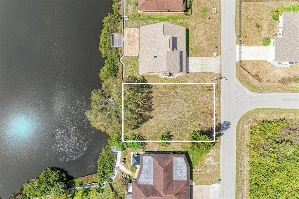 This aerial view shows a vacant, rectangular residential lot situated between two houses and water — 12029 CORSICA LANE, NORTH PORT, FL