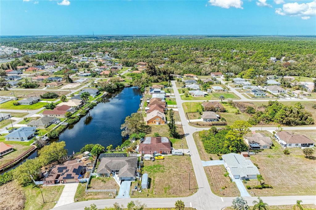 An aerial view shows a residential neighborhood with a central pond and surrounding houses — 12029 CORSICA LANE, NORTH PORT, FL