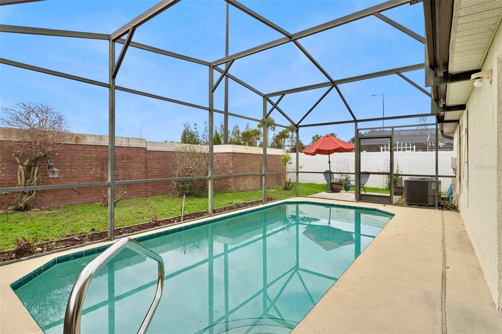 A swimming pool enclosed by a screened lanai sits in a backyard with a brick wall — 3195 WHOOPING CRANE RUN, KISSIMMEE, FL
