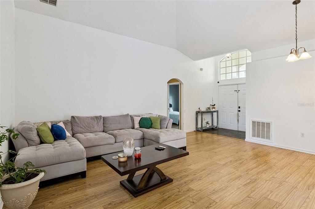 A living room with a gray sectional sofa, wood-look flooring, and a high vaulted ceiling — 3195 WHOOPING CRANE RUN, KISSIMMEE, FL