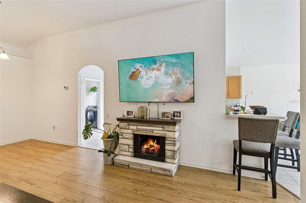 A living room features a stone fireplace, a wall-mounted television, and wood-look flooring — 3195 WHOOPING CRANE RUN, KISSIMMEE, FL