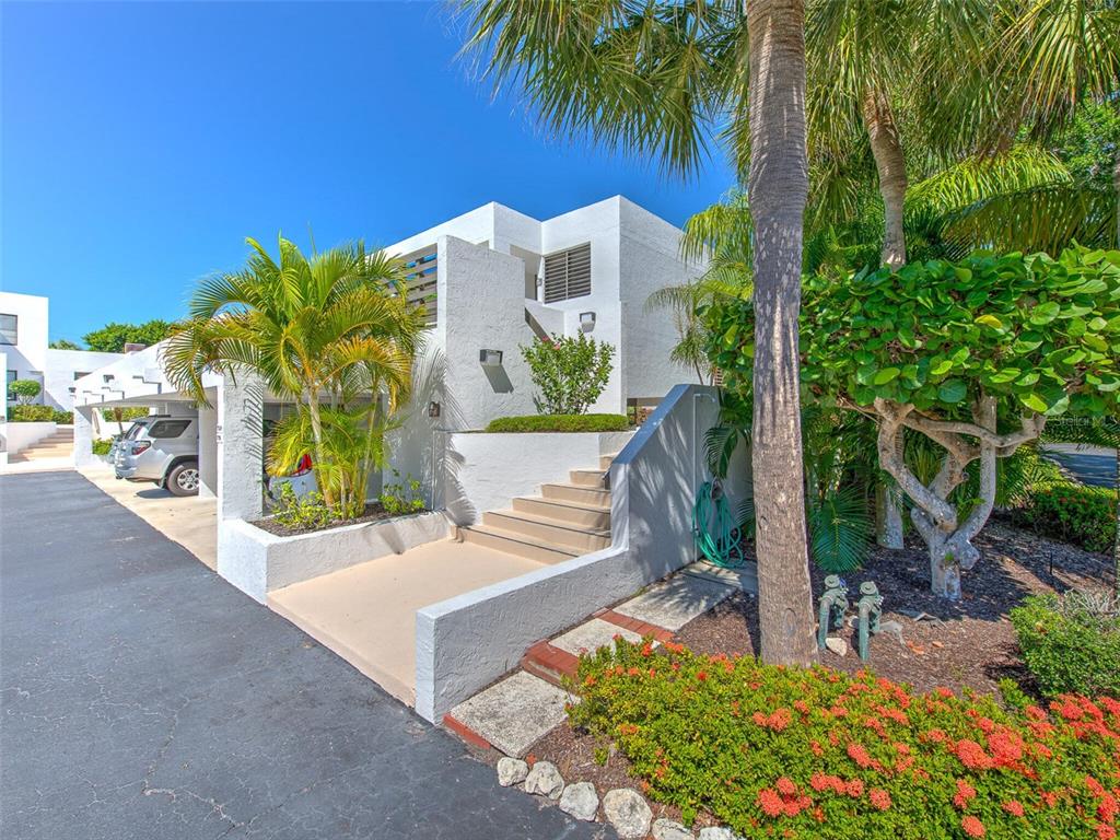A white multi-level building with a staircase, palm trees, and a covered parking area — 720 BAYPORT WAY UNIT 720, LONGBOAT KEY, FL