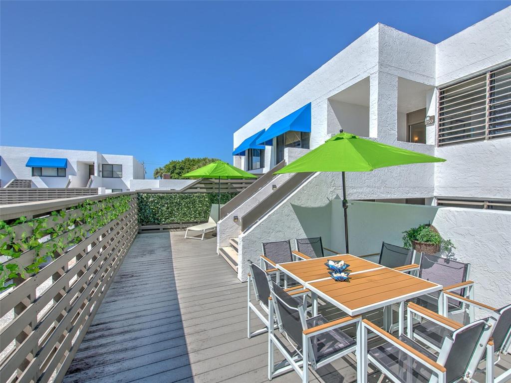 An outdoor deck features a dining set, a green umbrella, and a privacy fence — 720 BAYPORT WAY UNIT 720, LONGBOAT KEY, FL