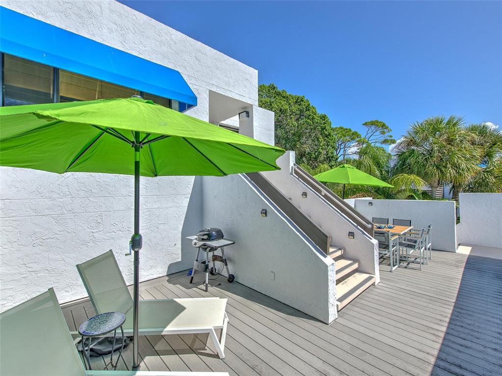 A wooden deck features a green umbrella, lounge chairs, a grill, and outdoor stairs — 720 BAYPORT WAY UNIT 720, LONGBOAT KEY, FL