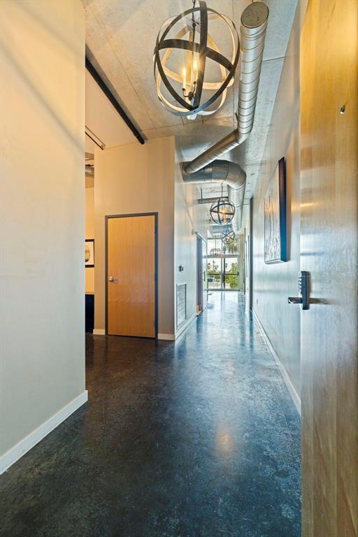 A hallway with concrete floors, exposed ductwork, and spherical pendant lights leads toward a window — 101 S 12TH STREET UNIT 302, TAMPA, FL