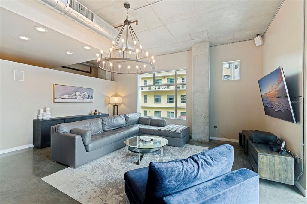 A modern living room features a grey sectional sofa, a chandelier, and concrete ceilings — 101 S 12TH STREET UNIT 302, TAMPA, FL