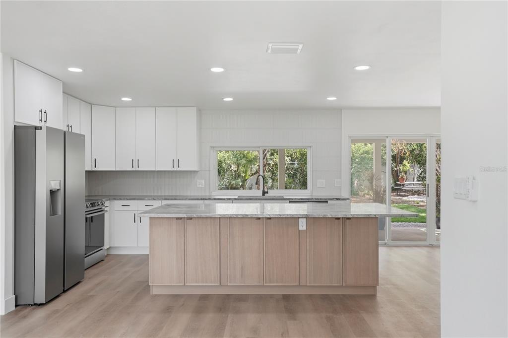 A modern kitchen features white cabinetry, a light wood island, and a view of the backyard — 2235 ANASTASIA WAY S, ST PETERSBURG, FL