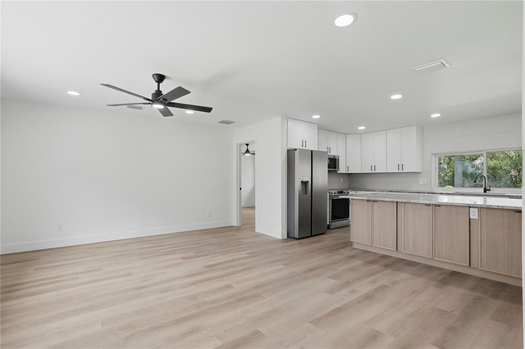 A modern kitchen and living area feature light wood flooring, white cabinetry, and stainless appliances — 2235 ANASTASIA WAY S, ST PETERSBURG, FL