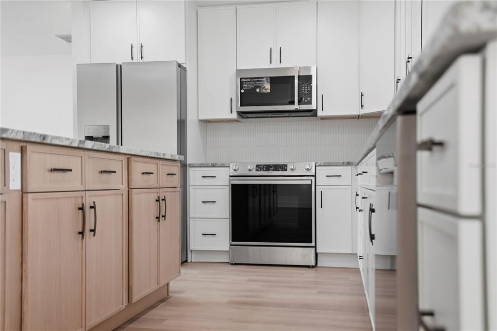 A modern kitchen features white upper cabinets, light wood lower cabinets, and stainless steel appliances — 2235 ANASTASIA WAY S, ST PETERSBURG, FL