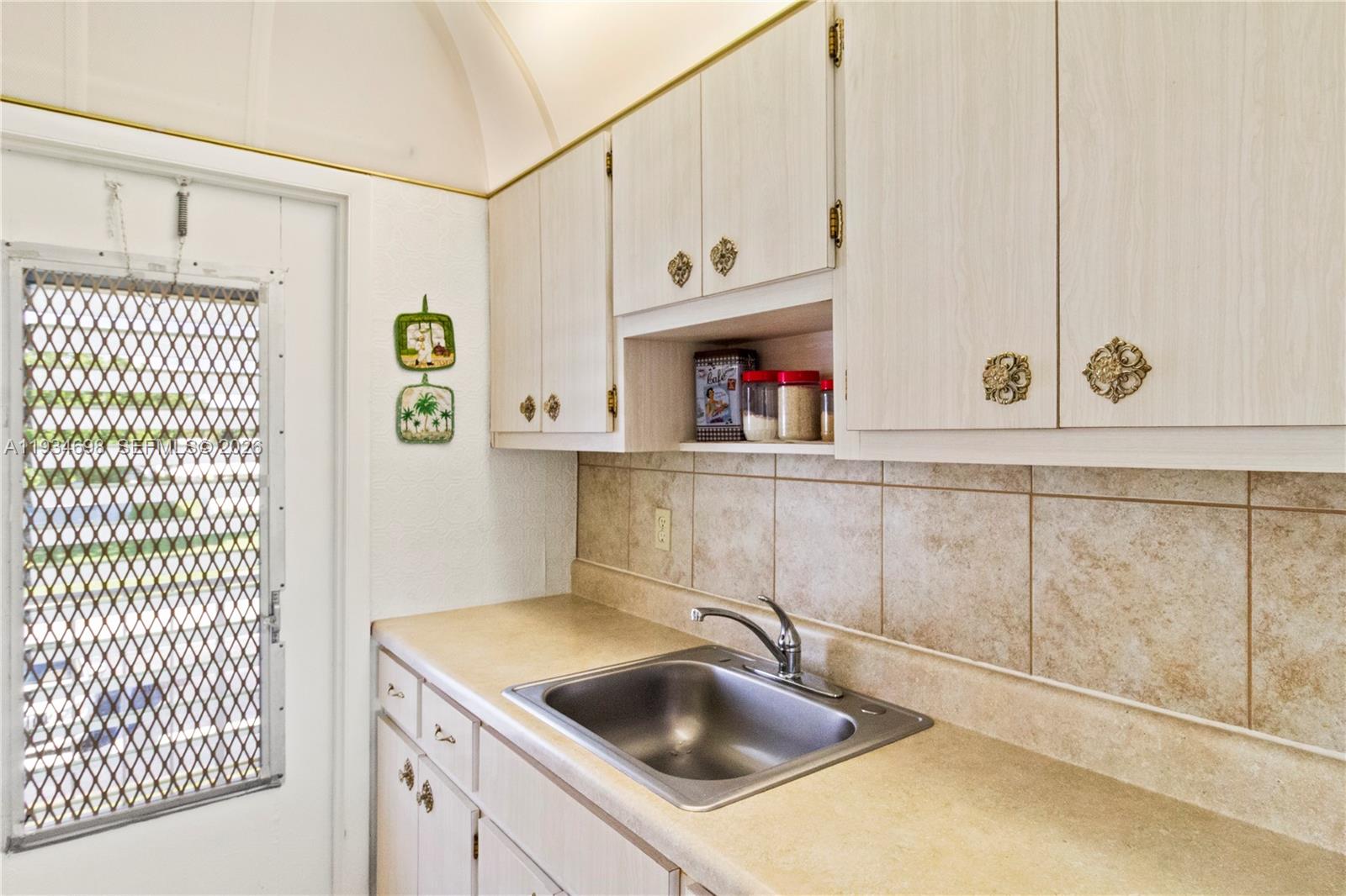 A kitchen features light wood cabinets, a stainless steel sink, and tan tile backsplash — 2850 W Golf Blvd # 211, Pompano Beach FL 33064, POMPANO BEACH, FL