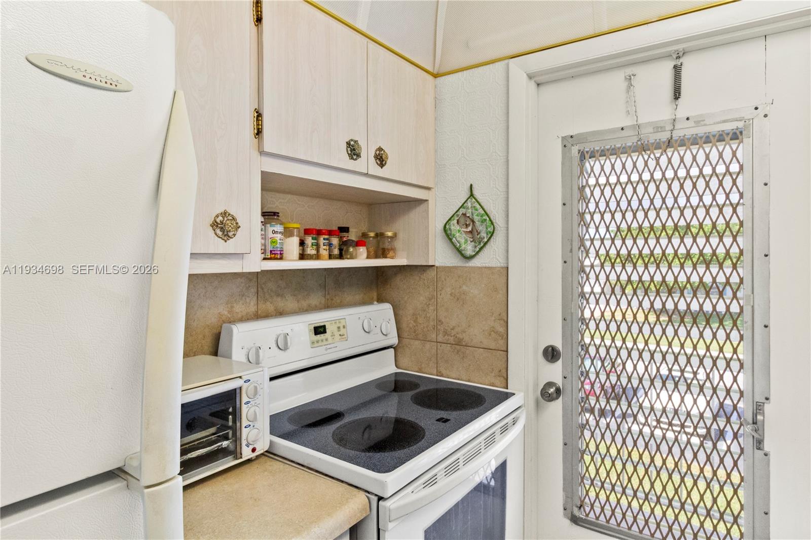 A kitchen features white cabinets, a glass-top stove, a refrigerator, and a screen door — 2850 W Golf Blvd # 211, Pompano Beach FL 33064, POMPANO BEACH, FL
