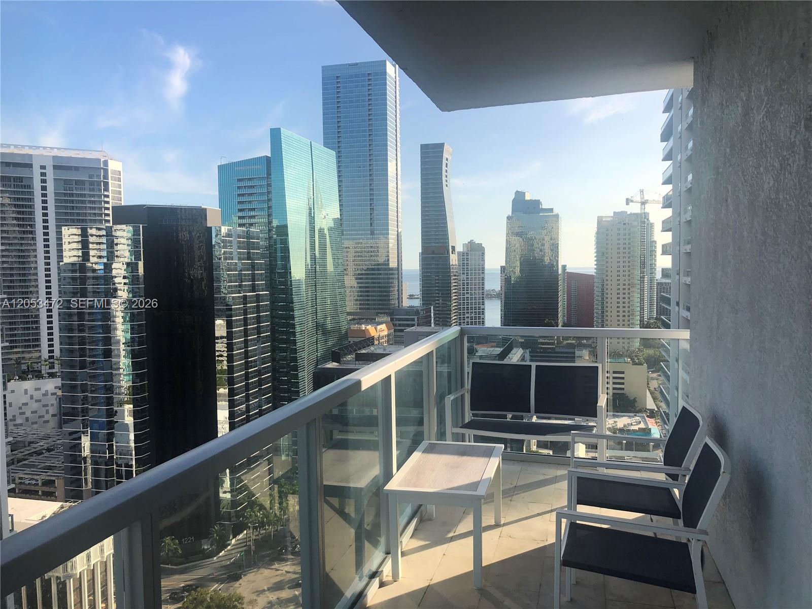 A balcony with outdoor furniture overlooks a dense urban skyline of glass skyscrapers — 1050 Brickell Ave # 2910, Miami FL 33131, MIAMI, FL