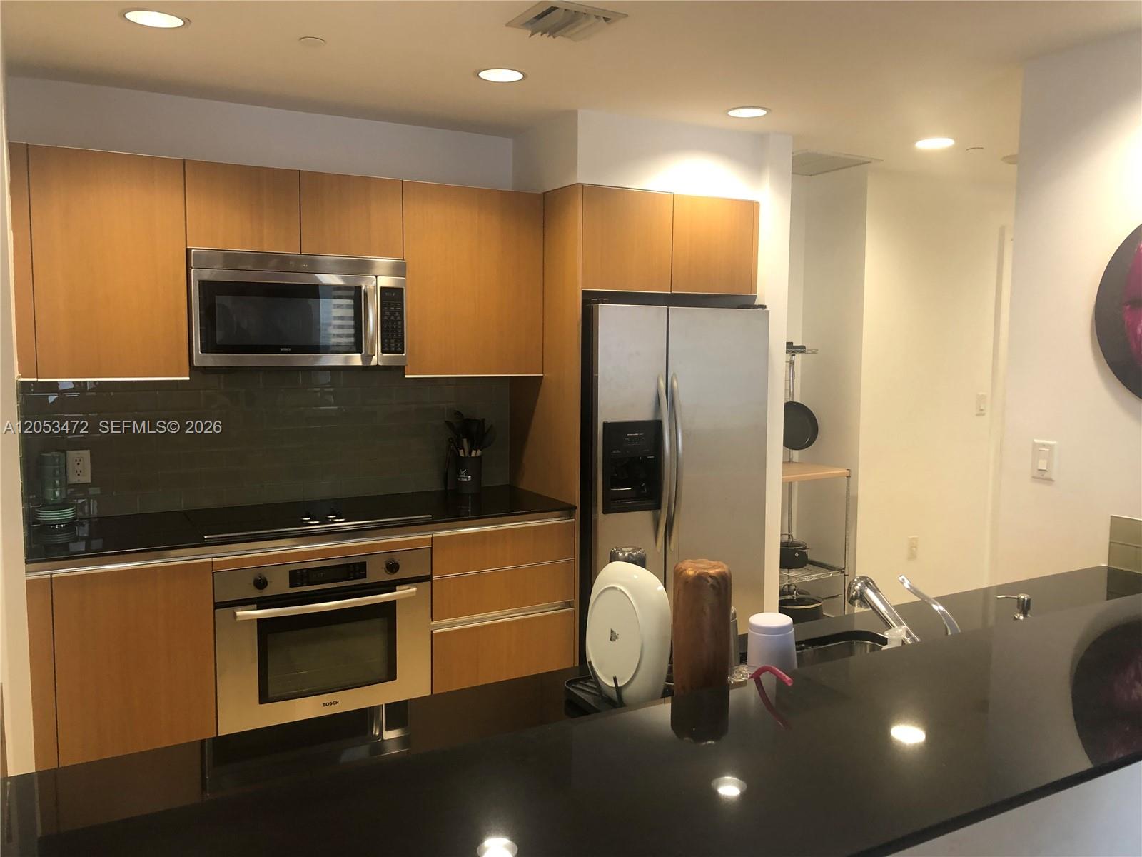 A modern kitchen features light wood cabinets, stainless steel appliances, and black granite countertops — 1050 Brickell Ave # 2910, Miami FL 33131, MIAMI, FL
