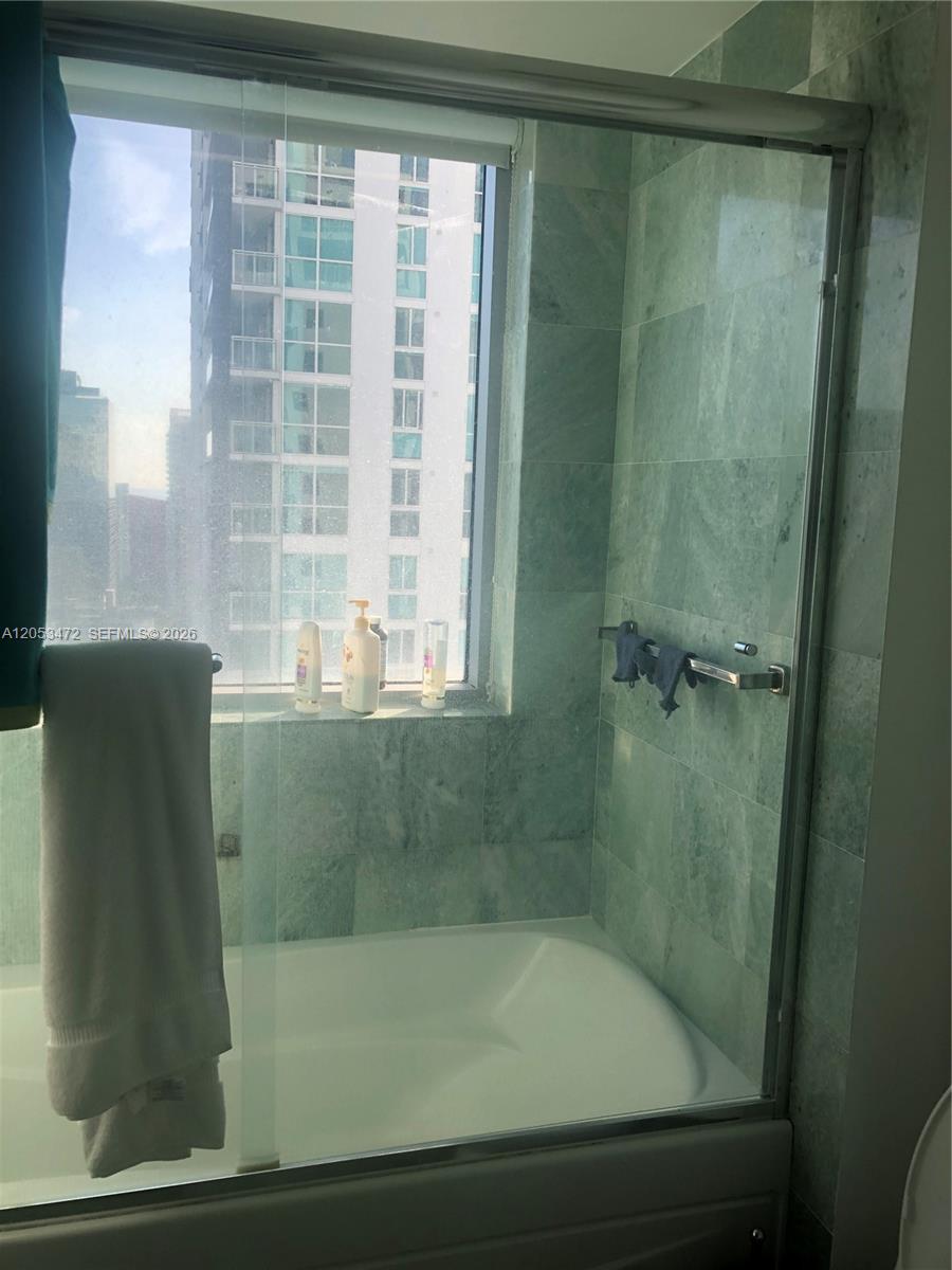 A bathroom features a white bathtub, a glass shower door, and green tiled walls — 1050 Brickell Ave # 2910, Miami FL 33131, MIAMI, FL