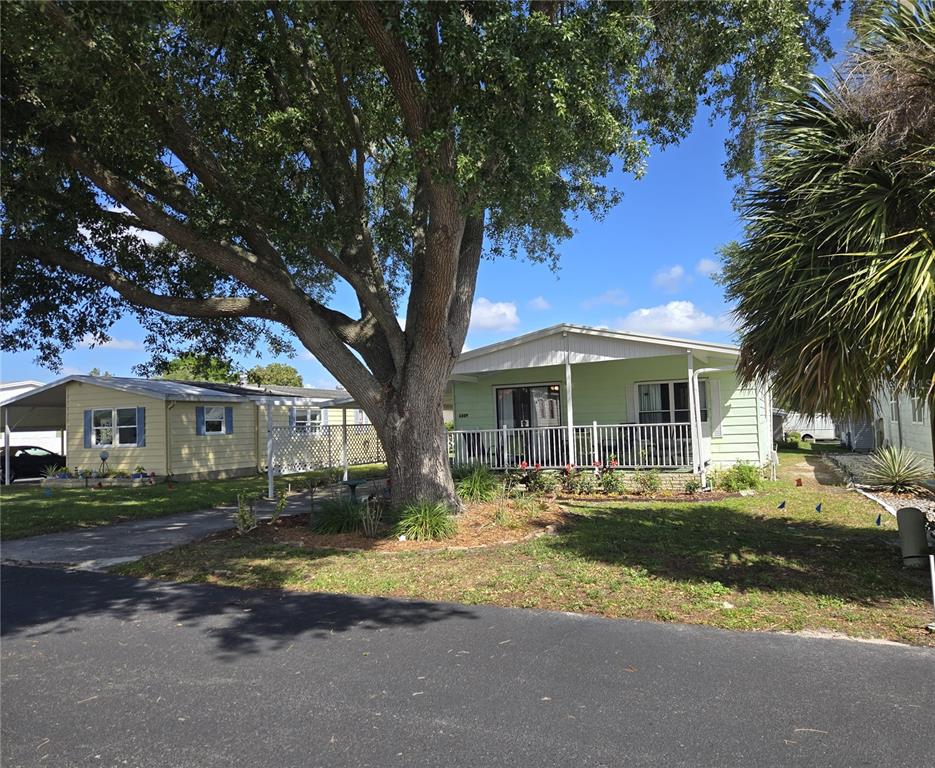 A light green manufactured home with a front porch sits beside a large oak tree — 6309 GROVE POINTE DRIVE SE, WINTER HAVEN, FL