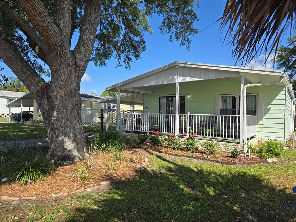 A light green manufactured home features a covered front porch and a large oak tree — 6309 GROVE POINTE DRIVE SE, WINTER HAVEN, FL