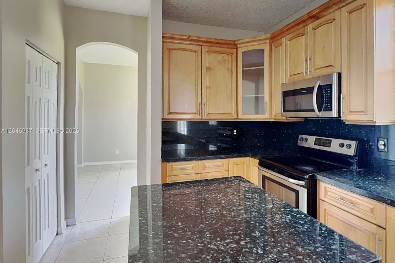 A kitchen features light wood cabinets, black granite countertops, and a central island — WESTON, FL